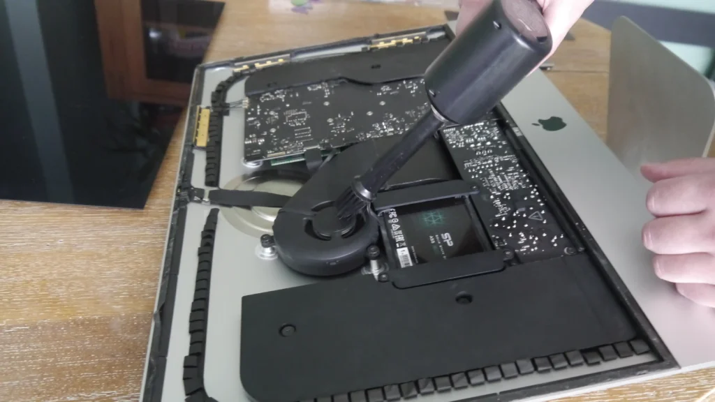 Dépoussiérage de l'intérieur de l'iMac avec l'outil adapté.